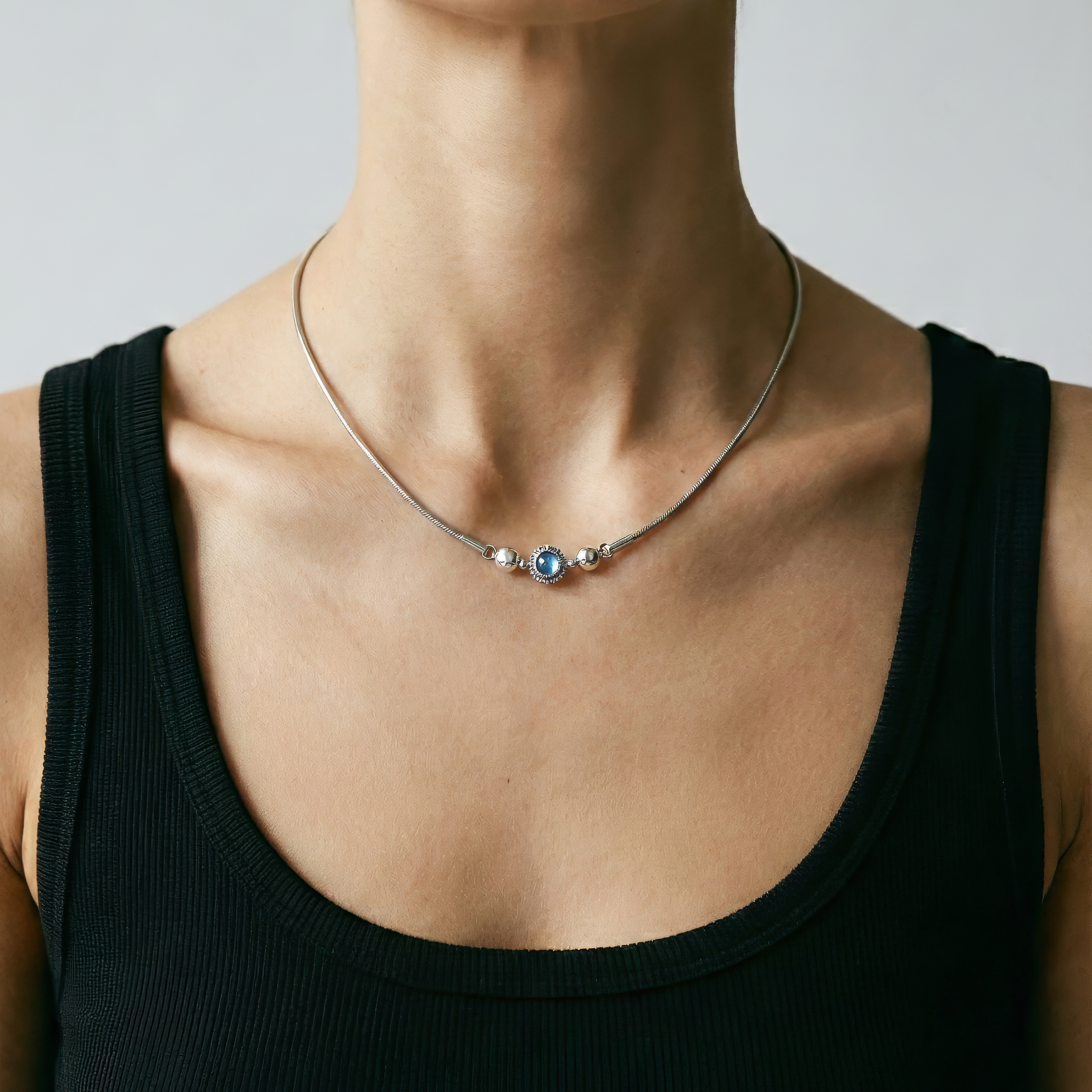 Person wearing a black tank top and a delicate necklace with a gray background
