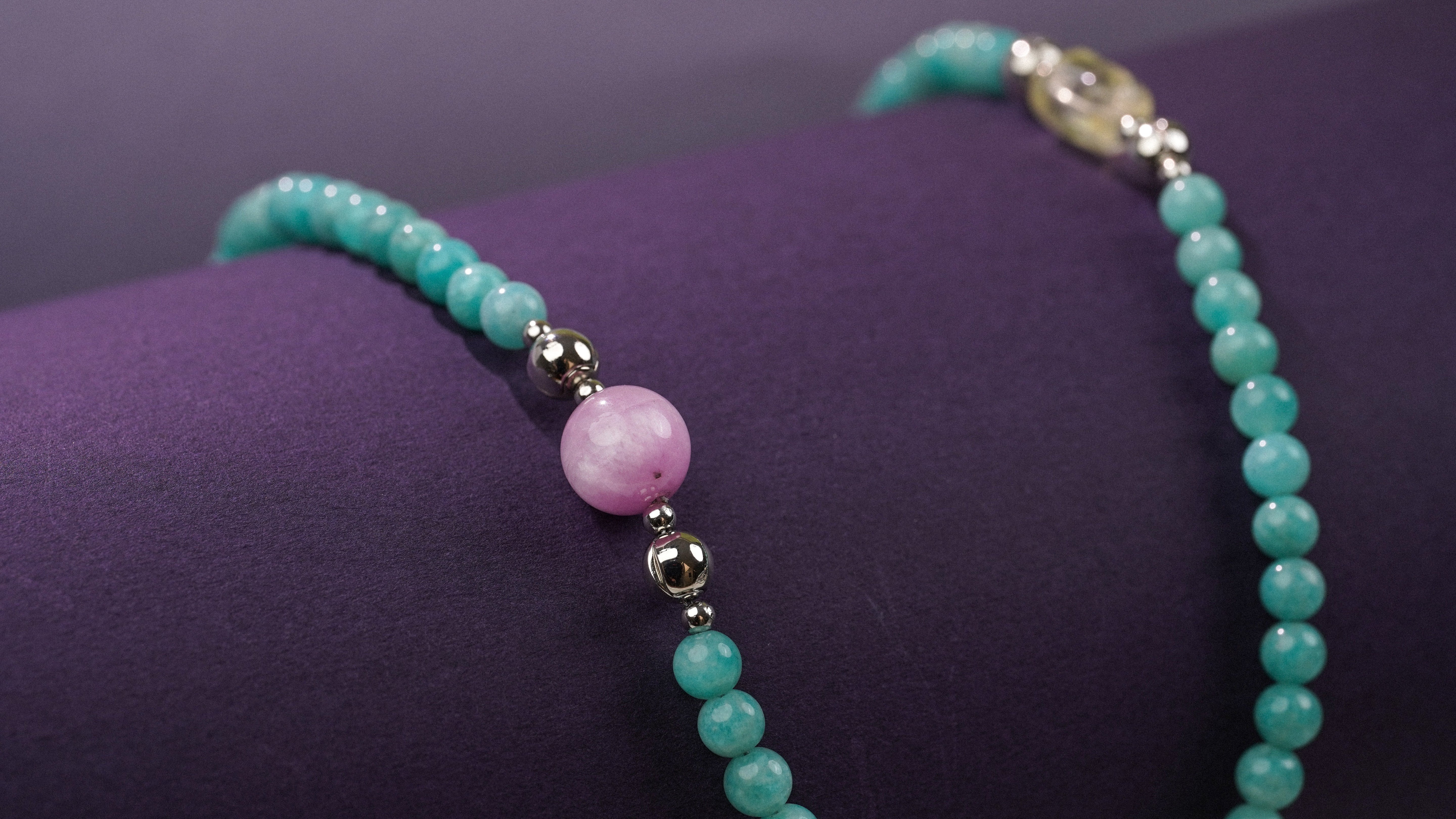 Turquoise beaded bracelet with a pink bead on a purple surface