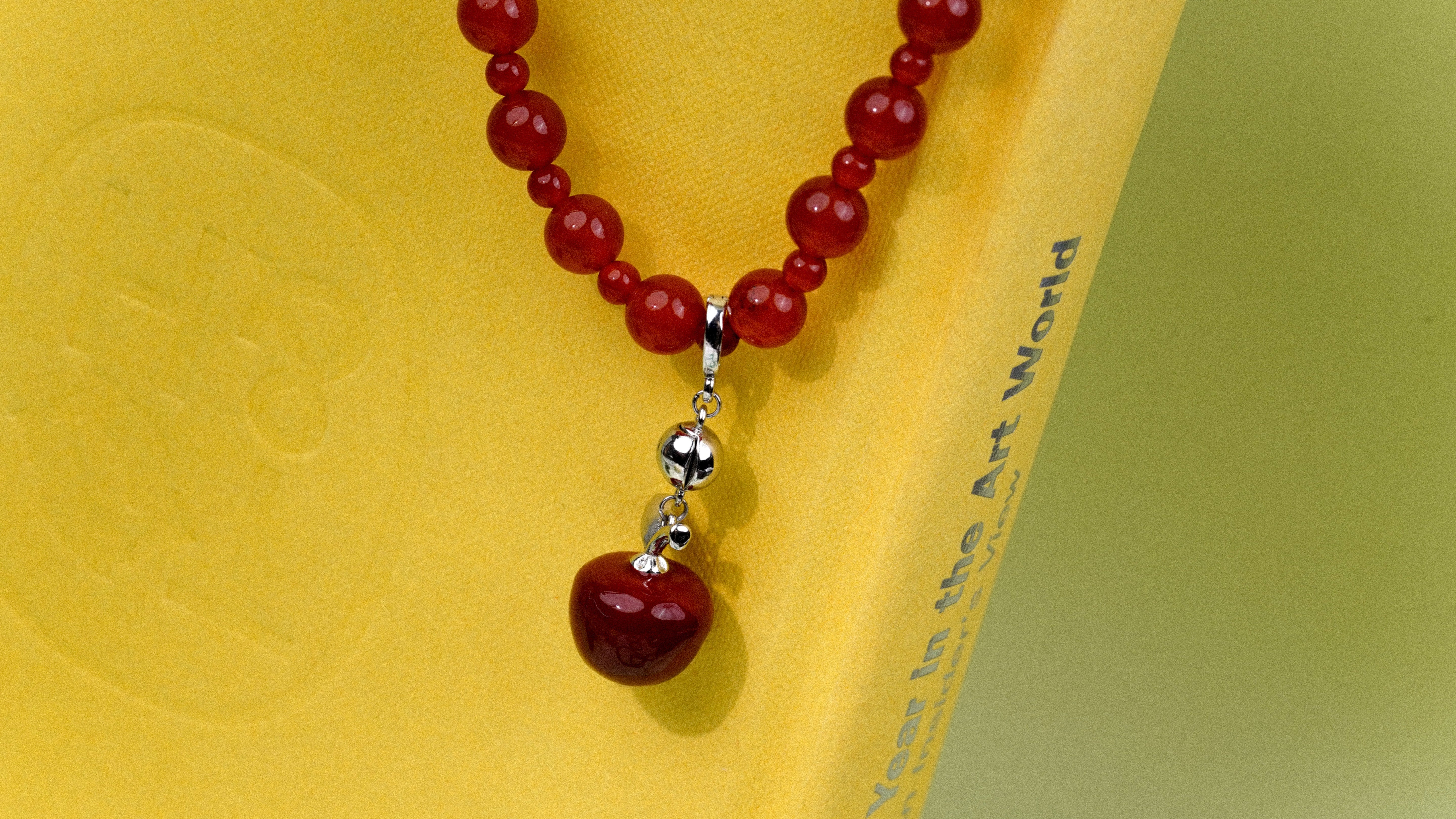 Red beaded necklace with a silver pendant on a yellow background