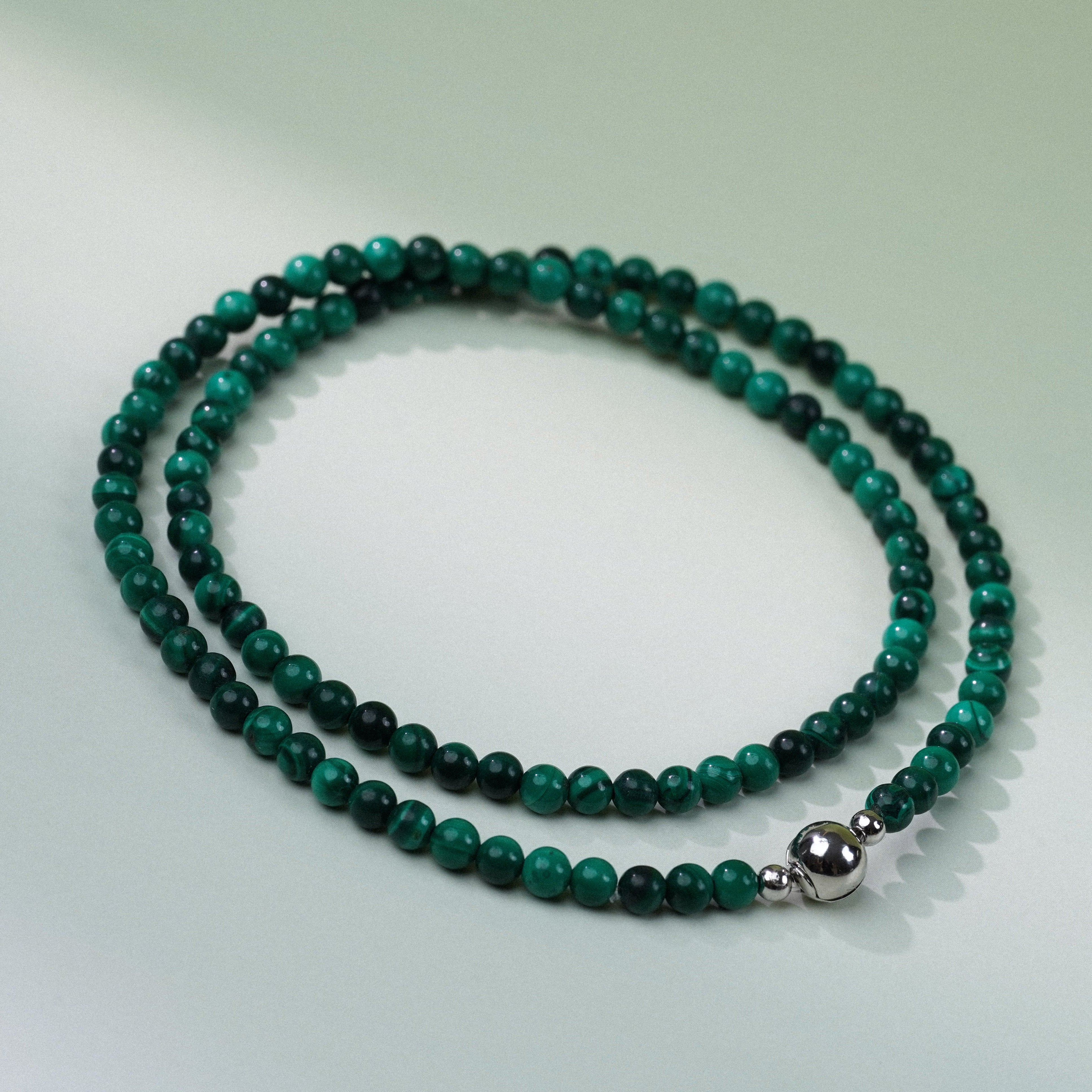 Green beaded necklace with a silver clasp on a light gray background